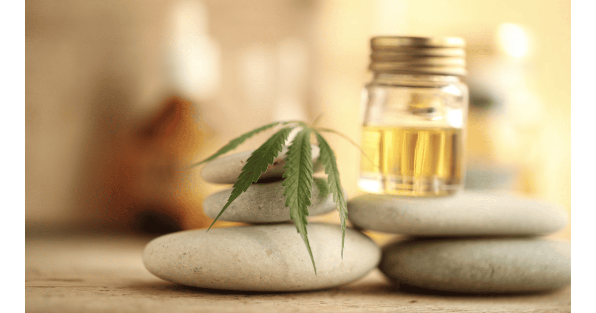 Aceite de CBD en frasco pequeño con hoja de cáñamo, sobre piedras lisas en un fondo difuso.