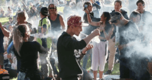 Personas disfrutando de una fiesta en verano con humo y música en un parque.